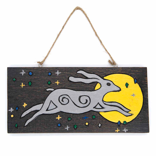 Front view of moon hare wood sign on white background, grey hare with spiral body markings leaping toward a yellow moon, Indo