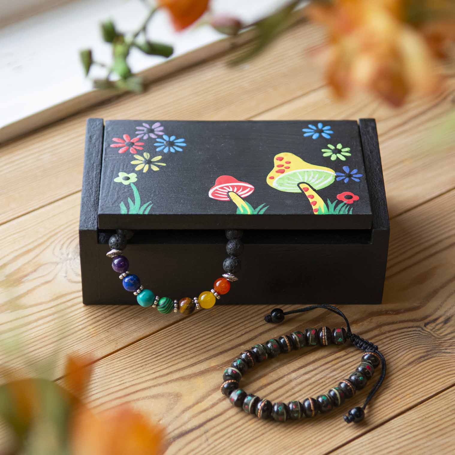 Black painted wooden mushroom box closed on a wooden surface with jewellery beside it, Indonesia