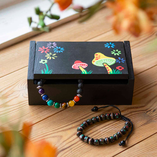 Black painted wooden mushroom box closed on a wooden surface with jewellery beside it, Indonesia