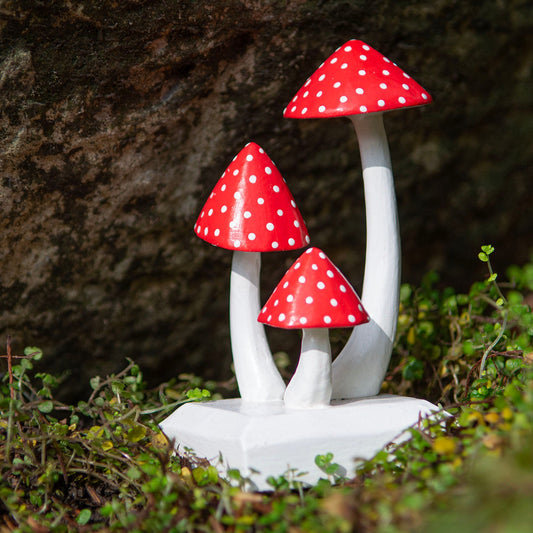Carved wooden fly agaric mushroom cluster, red caps with white spots, photographed outdoors against rock