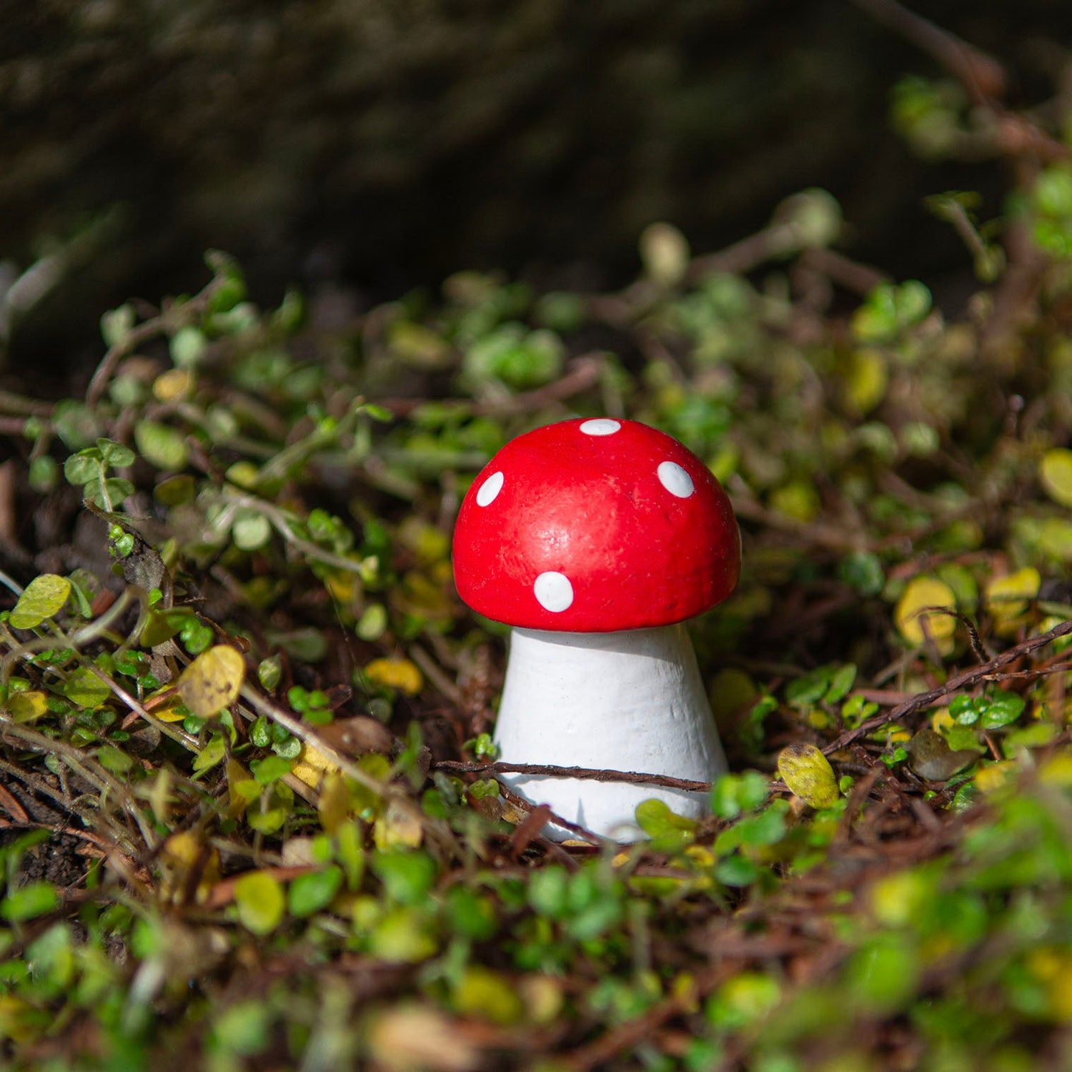 Mini carved wooden fly agaric mushroom with red cap and white spots nestled in outdoor moss, Indonesia