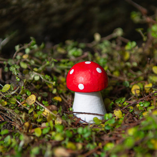Mini carved wooden fly agaric mushroom with red cap and white spots nestled in outdoor moss, Indonesia