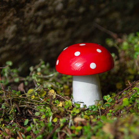 Small carved wooden fly agaric mushroom with red domed cap and white spots standing in outdoor moss