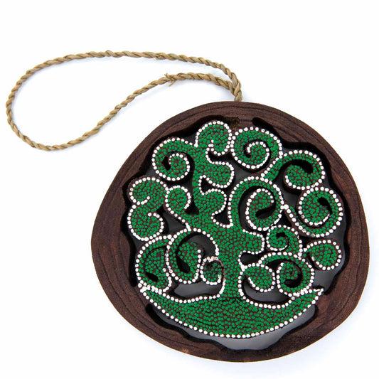 Front view of dot-painted tree of life wood disc with braided twine loop, green and white dots on dark wood, white background