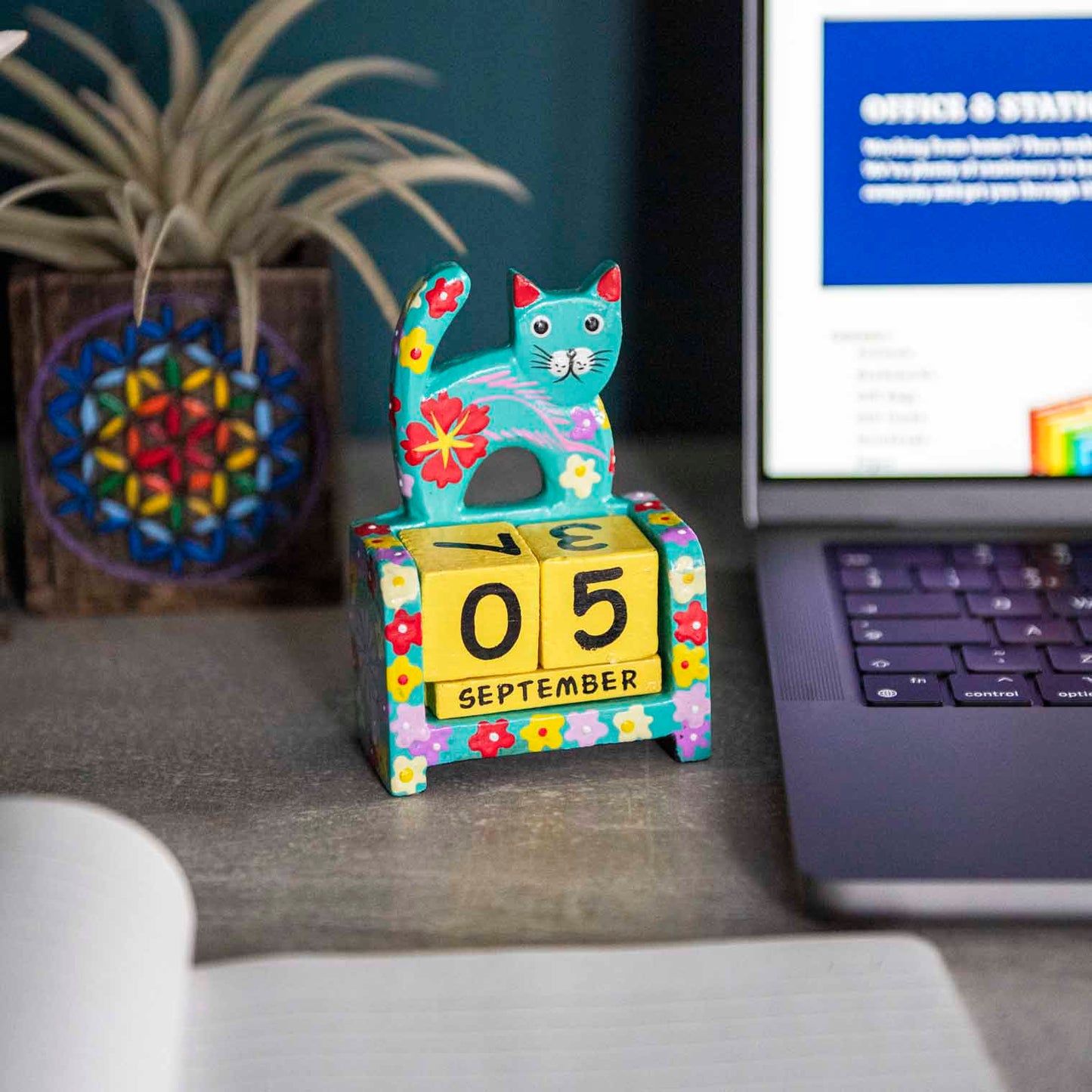 Teal hand-painted wooden cat perpetual calendar on a desk showing September date, Indonesia