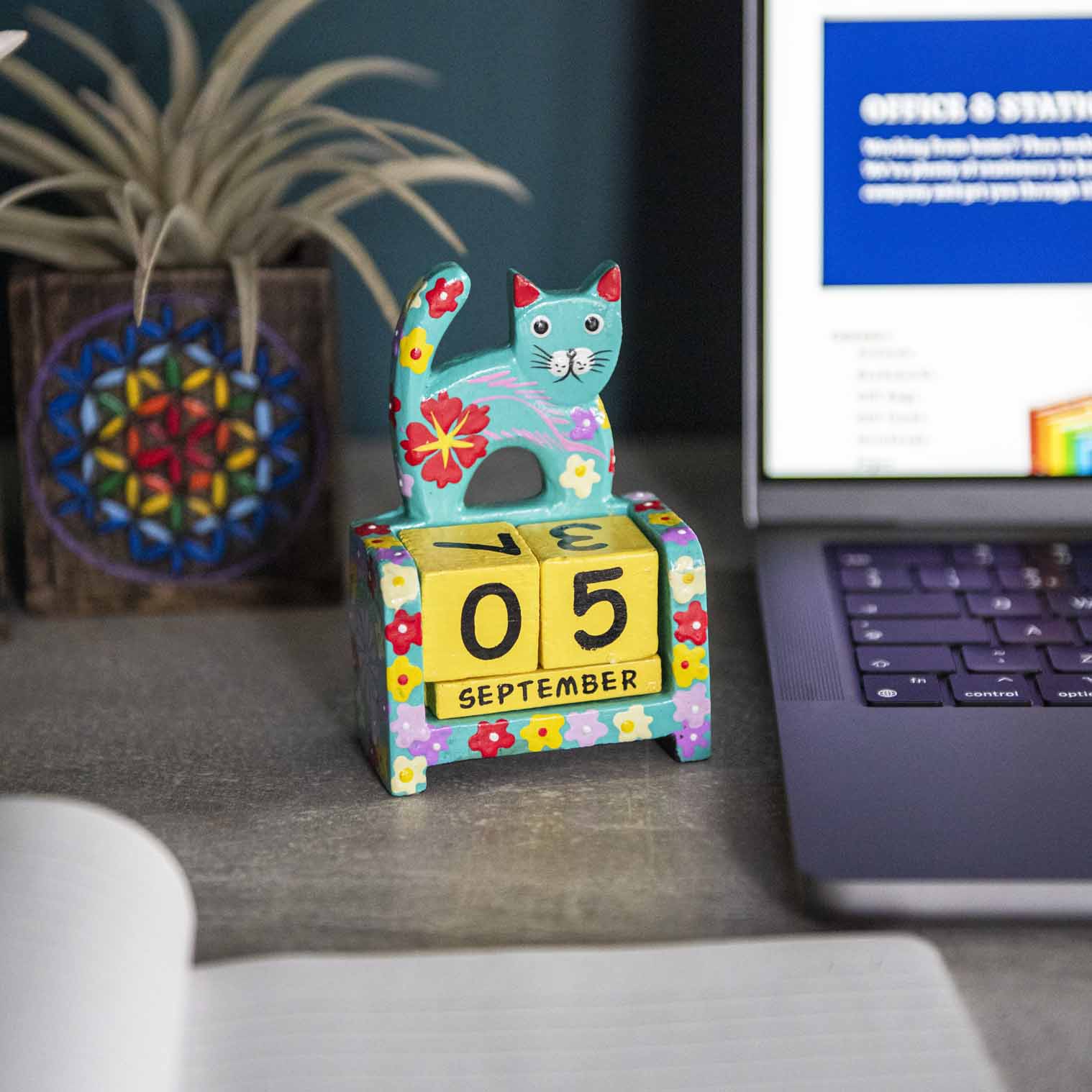 Teal hand-painted wooden cat perpetual calendar on a desk showing September date, Indonesia