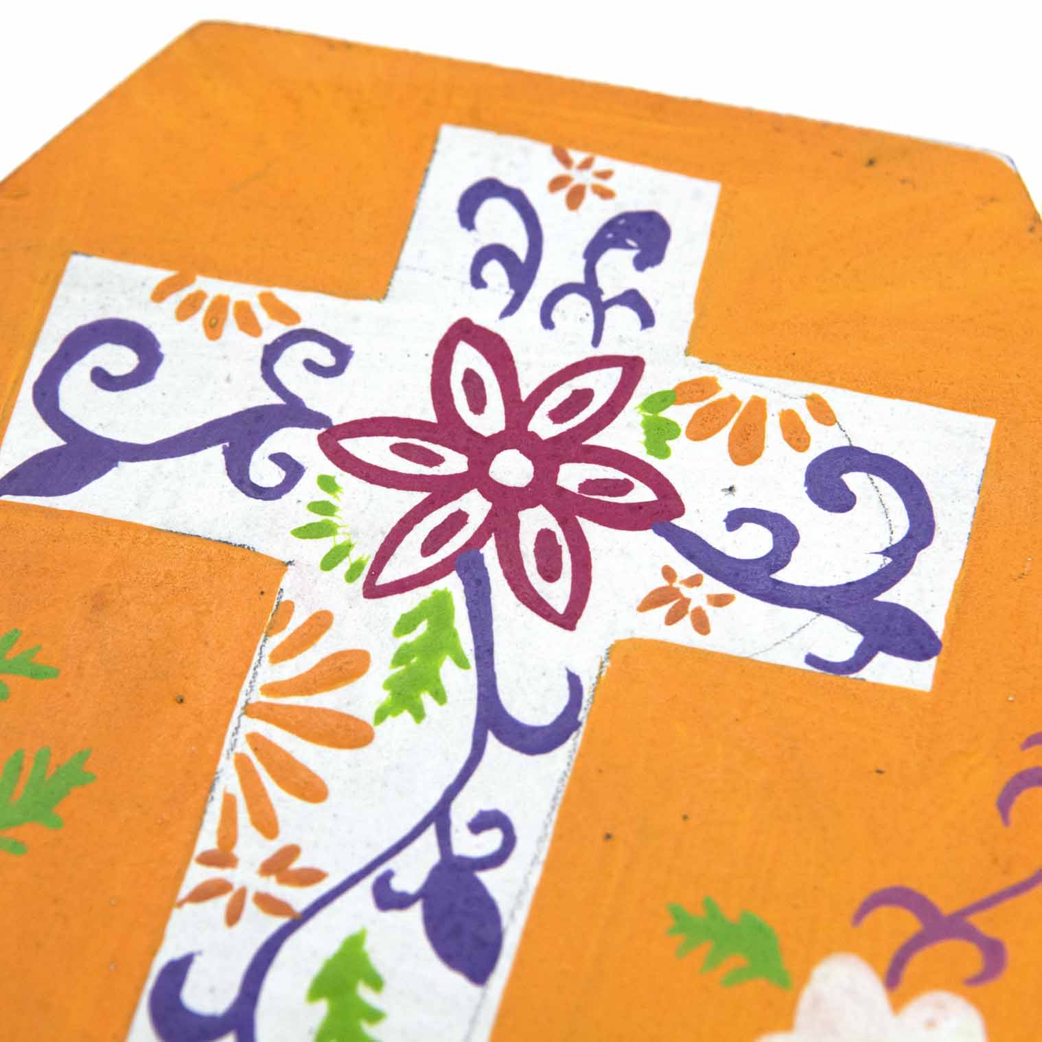 Close-up of hand-painted floral cross detail on orange wooden box lid, purple scrollwork and crimson flower