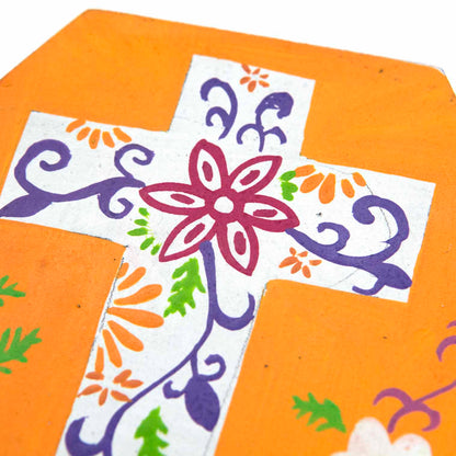 Close-up of hand-painted floral cross detail on orange wooden box lid, purple scrollwork and crimson flower