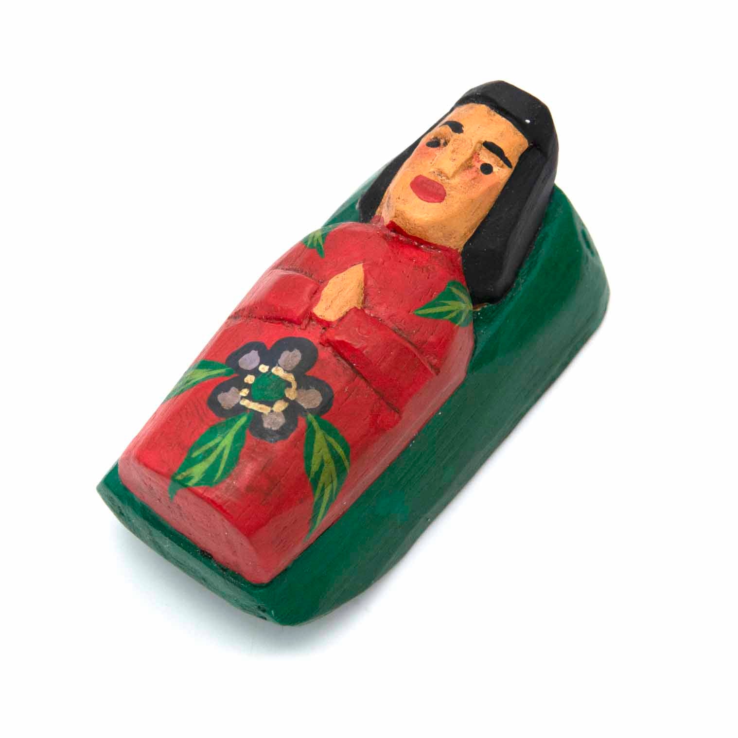 Carved wood baby Jesus in manger, angled view showing blocky form and hand-painted floral motif