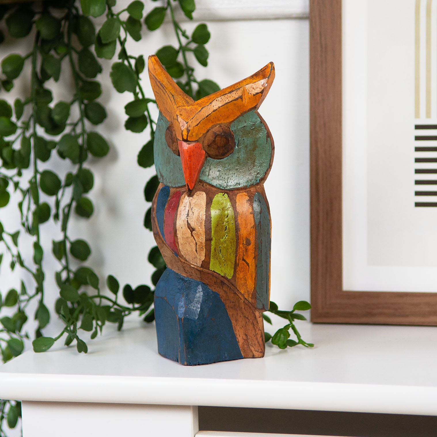 Rustic painted wooden owl carving on a white shelf, teal eyes and orange ears, Indonesia