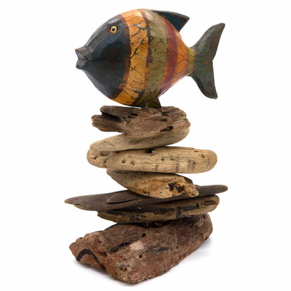 Painted wooden fish in orange and slate bands balanced on a stacked driftwood column, Indonesia