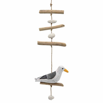 Full-length view of seagull hanging: driftwood sticks, white pebbles and painted bird on perch