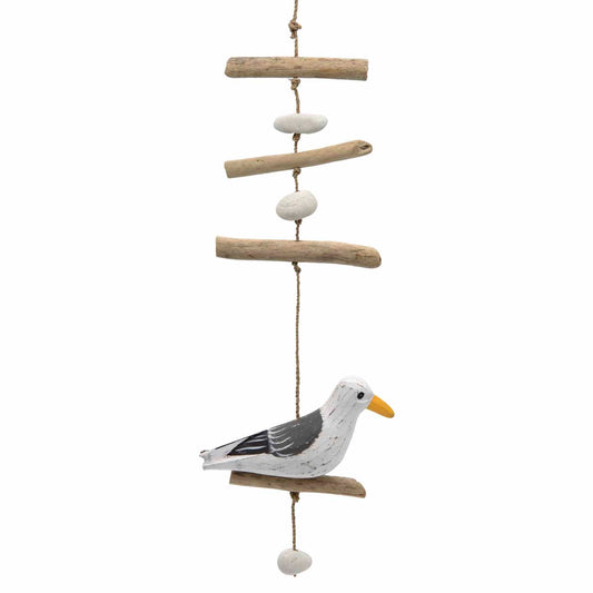 Full-length view of seagull hanging: driftwood sticks, white pebbles and painted bird on perch