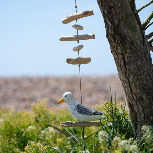 Hanging wooden seagull with driftwood sticks and pebbles on jute cord, outdoors against blue sky