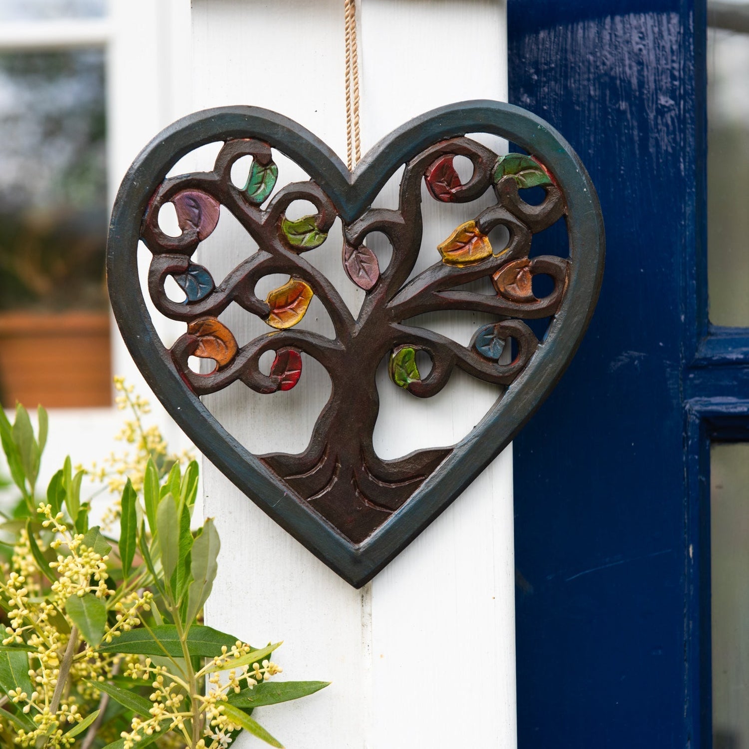 Heart-shaped Tree of Life wood plaque with autumn leaves hanging on a white exterior wall beside a blue door