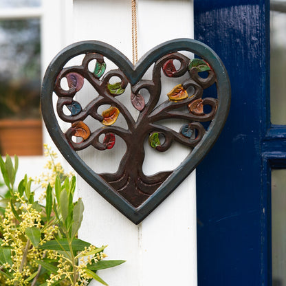 Heart-shaped Tree of Life wood plaque with autumn leaves hanging on a white exterior wall beside a blue door