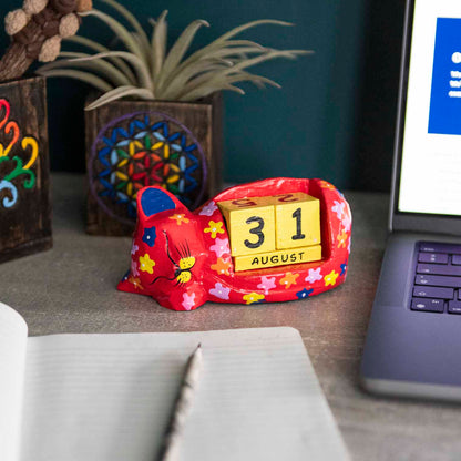 Red painted wooden sleeping cat perpetual calendar on a desk showing August date, Indonesia