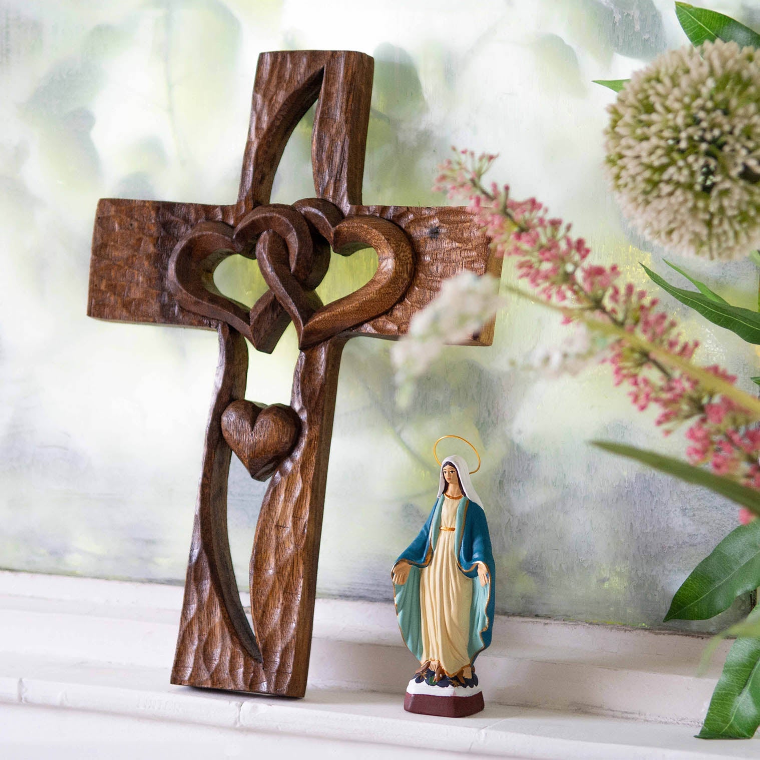 Carved wood cross with interlocking hearts, leaning against wall in lifestyle setting, Indonesia