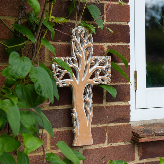 Whitewash tree cross plaque hanging on a red brick wall beside climbing plants, Indonesia