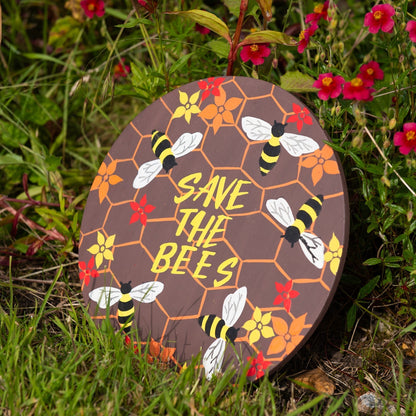 Round Save the Bees plaque resting among red and orange garden flowers, showing full painted surface