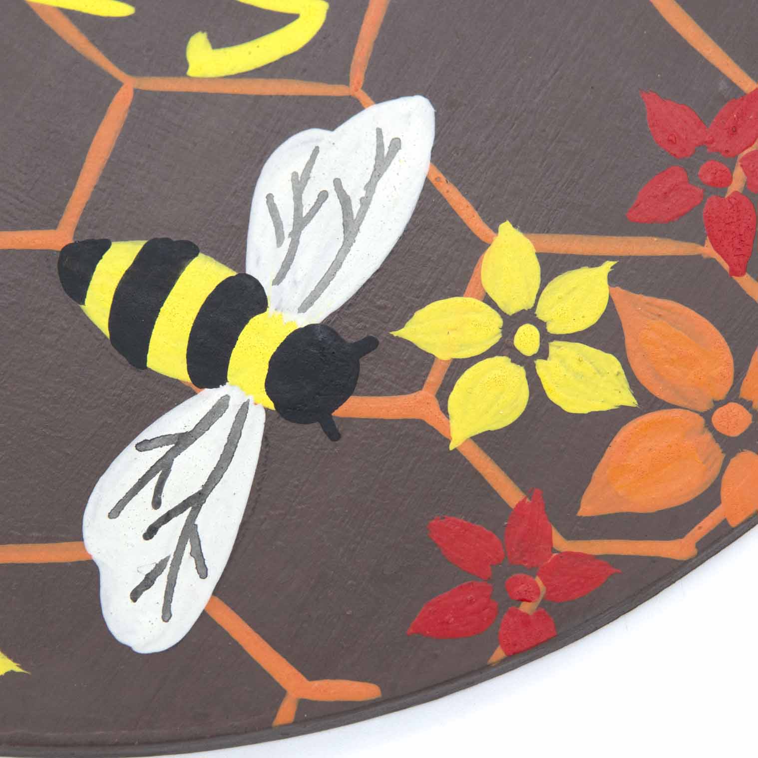 Close-up of hand-painted bee on Indonesian wood plaque showing yellow and black striped body and white wings