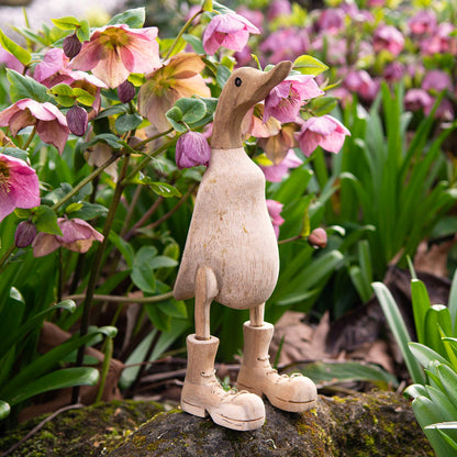 Natural unvarnished bamboo root duck with carved boots, photographed among hellebore flowers in a garden