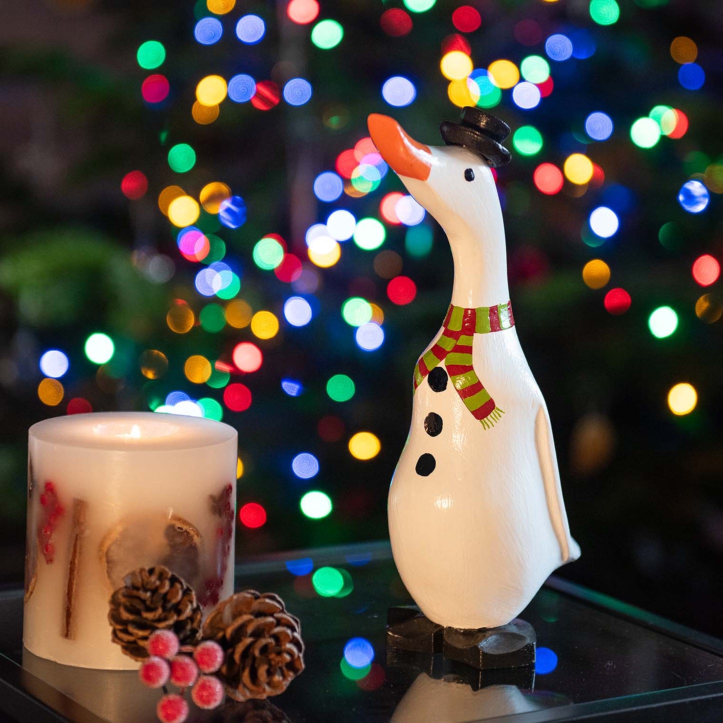 Snowman bamboo root duck with black top hat and striped scarf, photographed against Christmas tree bokeh lights