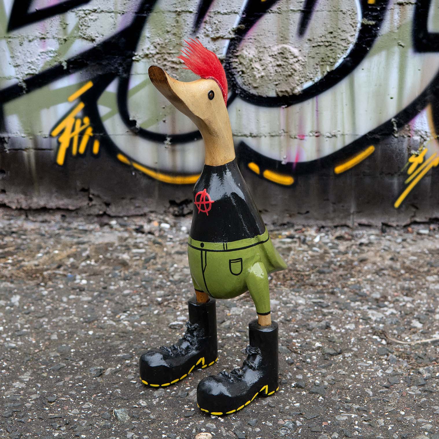 Punk bamboo root duck with red mohawk and black anarchy jacket, photographed against graffiti wall