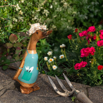 Gardening bamboo root duck with straw hat and teal apron, photographed in a garden border with flowers and a hand fork