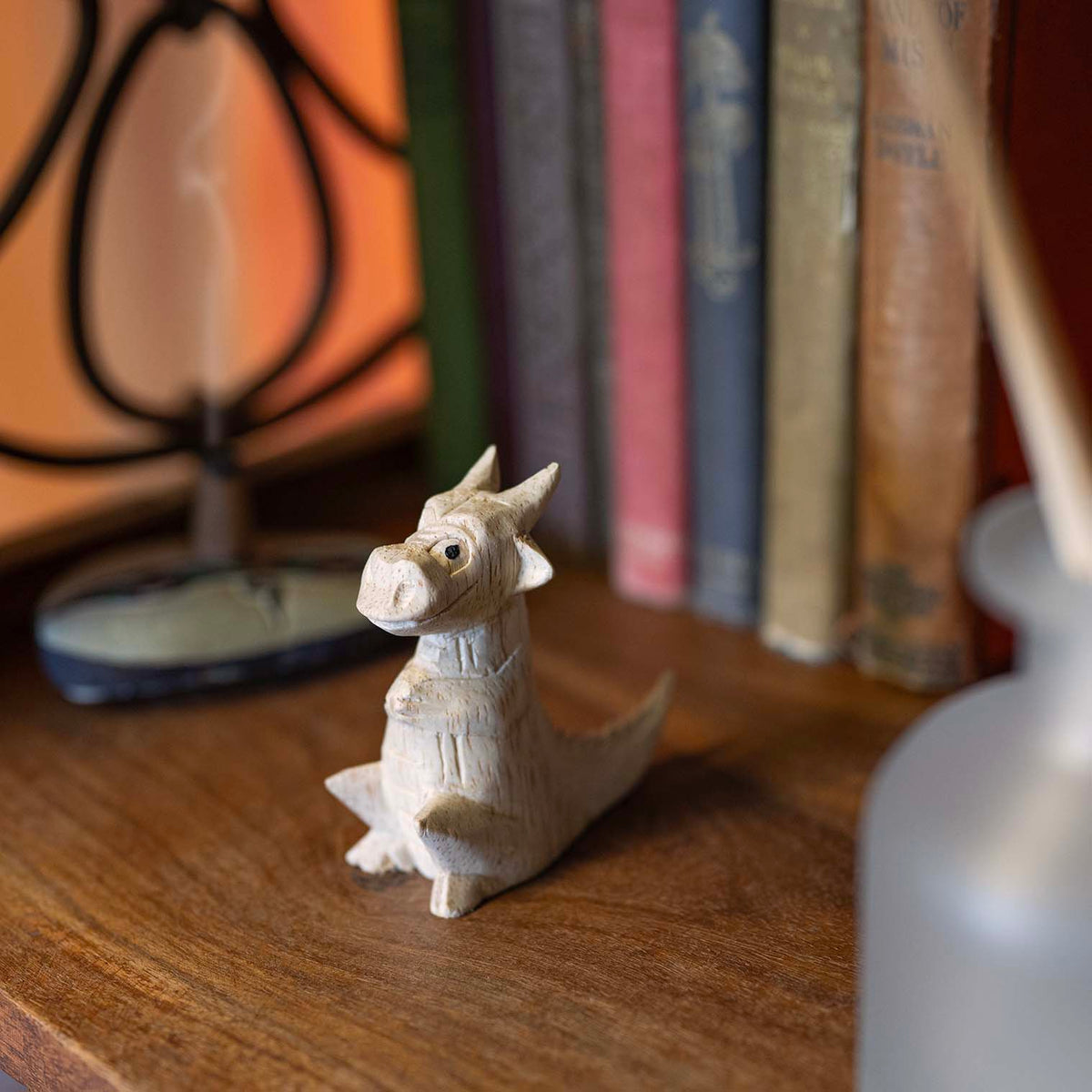 Pale Albizia wood mini dragon carving seated upright on wooden desk, herringbone spine detail visible