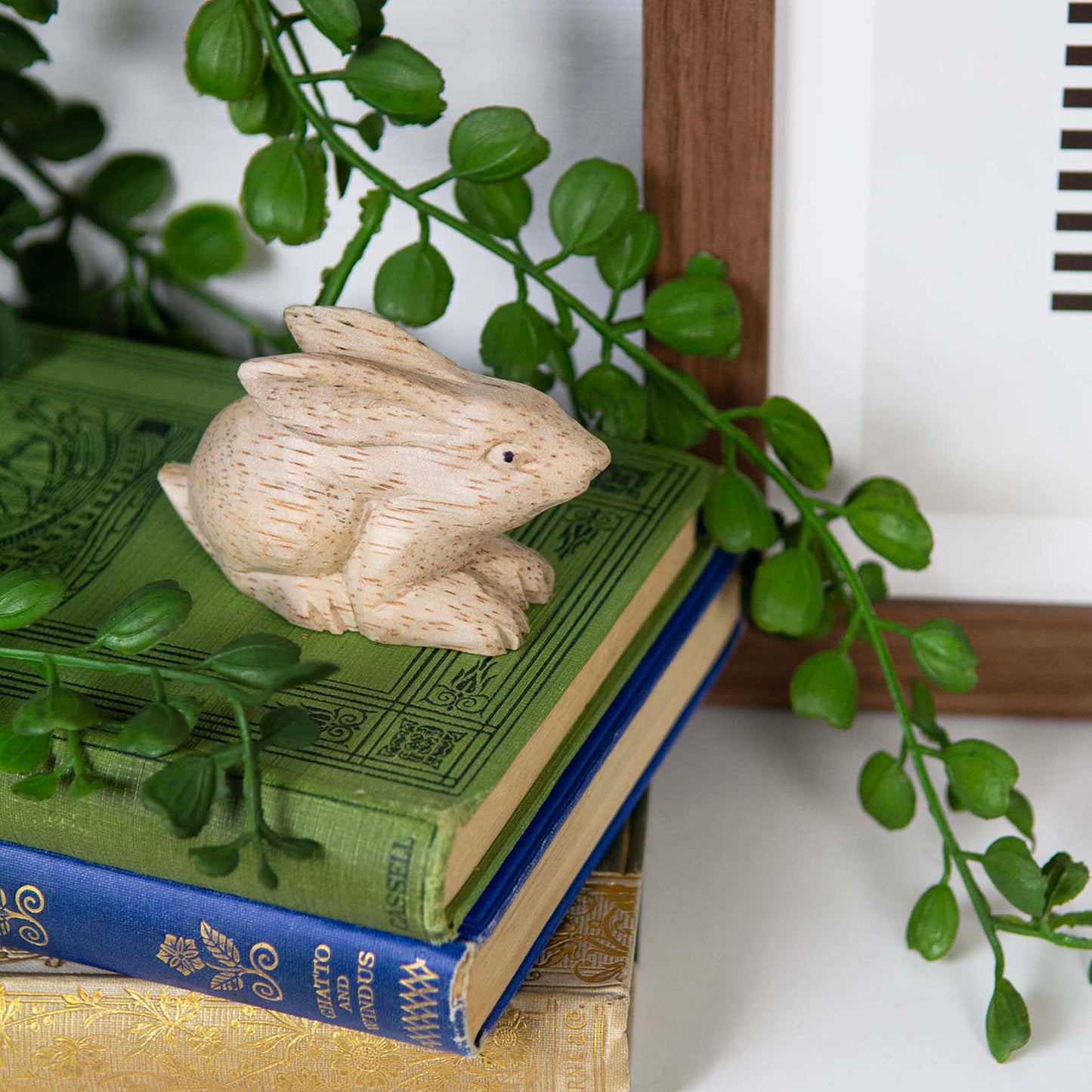 Mini pale wood rabbit carving on a stack of books beside a houseplant, Indonesia