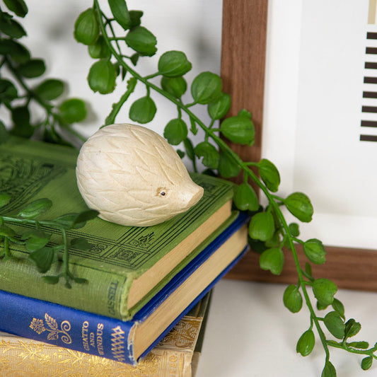 Mini pale wood hedgehog carving on a stack of books beside a houseplant, Indonesia