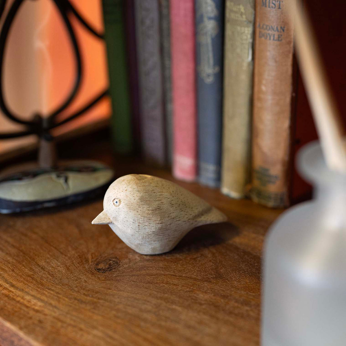 Pale wood hand-carved bird figurine with rounded body and pointed bill, displayed on wooden desk beside vintage books