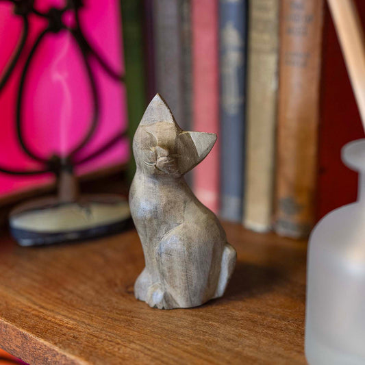 Pale Indonesian wood sitting cat carving with closed eyes and pointed ears, displayed on wooden desk