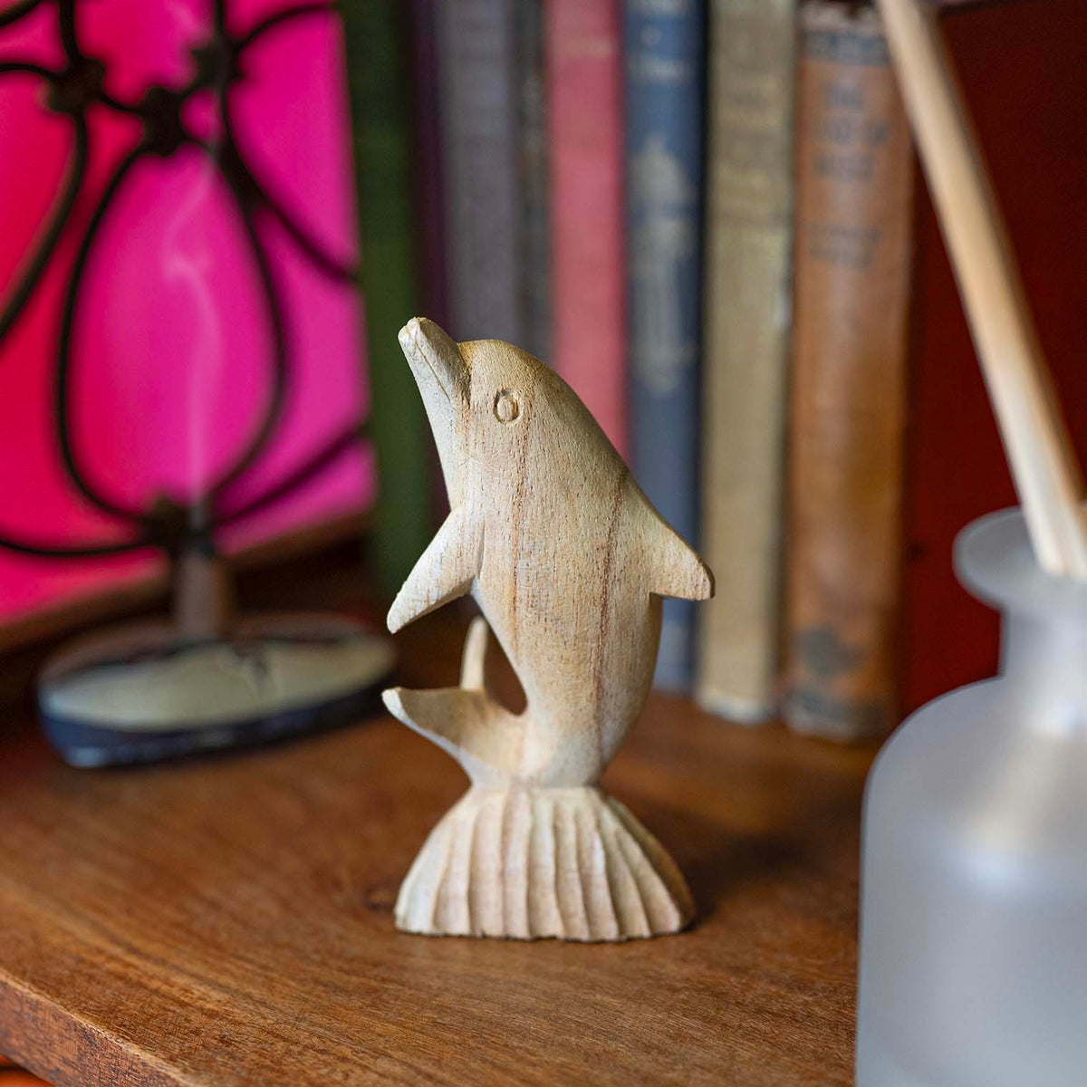 Hand-carved pale wood dolphin with lifted snout and defined fins, arching upward from a shell-textured wave base