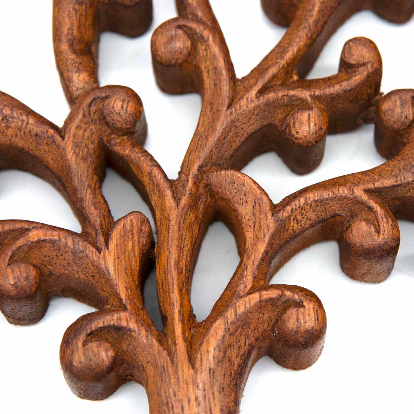 Close-up of carved branch tips on Indonesian Tree of Life plaque showing tight scrolls, buds and warm brown grain