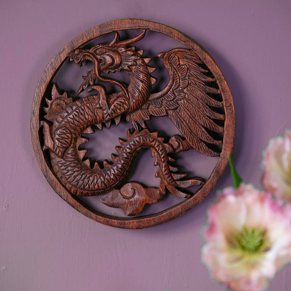 Circular wooden plaque with carved dragon in relief, wings spread and scales detailed, pierced cutwork showing through warm brown wood grain
