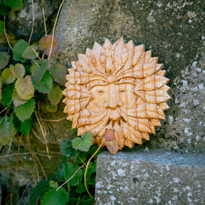 Round Green Man wood plaque with leaf-ringed face resting on a stone step among ivy, Indonesia