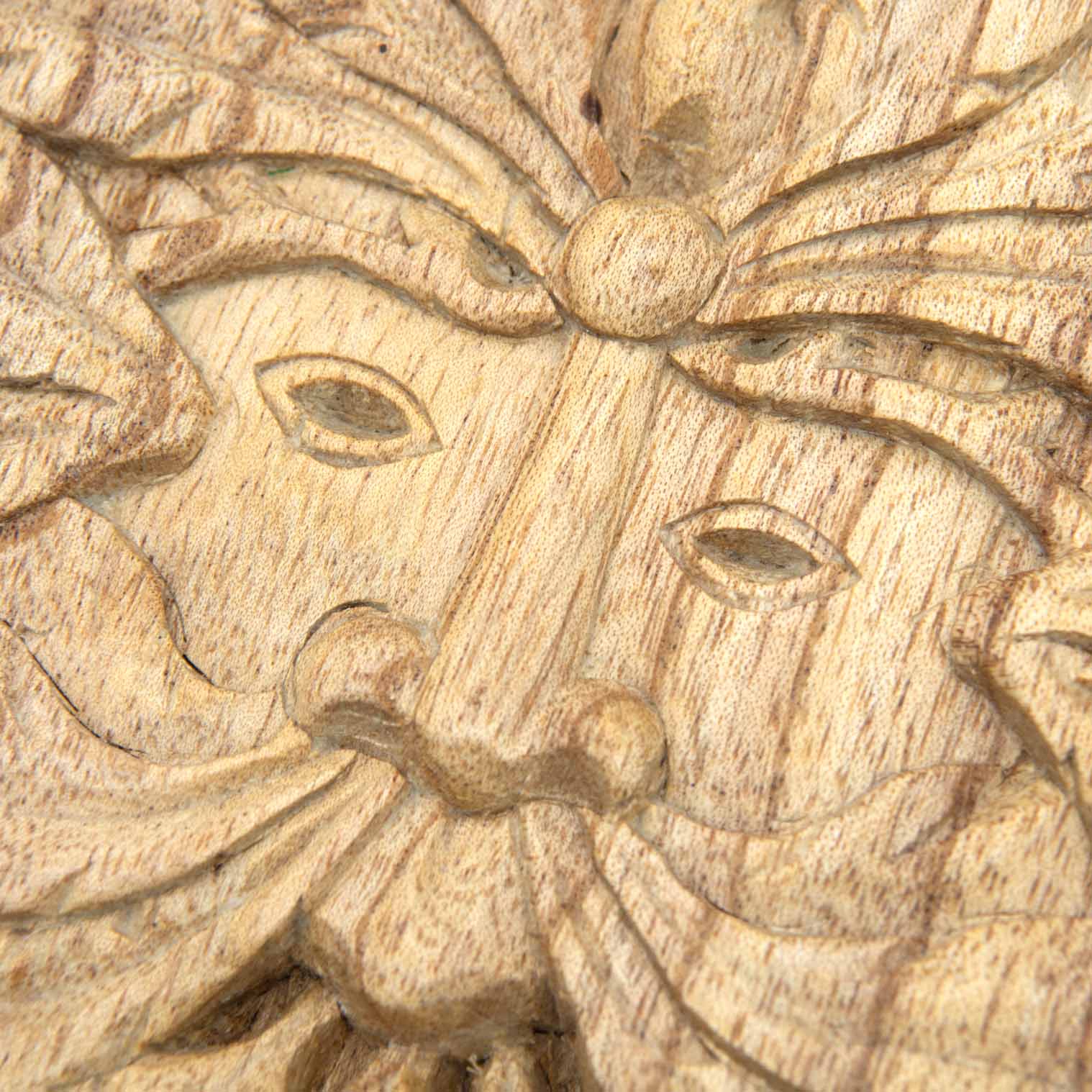 Close-up of Green Man face on Indonesian carved wood plaque showing eyes, nose and leaf beard in pale natural-stained wood