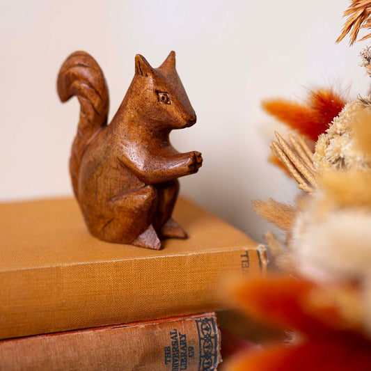 Hand-carved wooden squirrel in amber-brown wood, sitting upright with curved tail, displayed on stacked vintage books