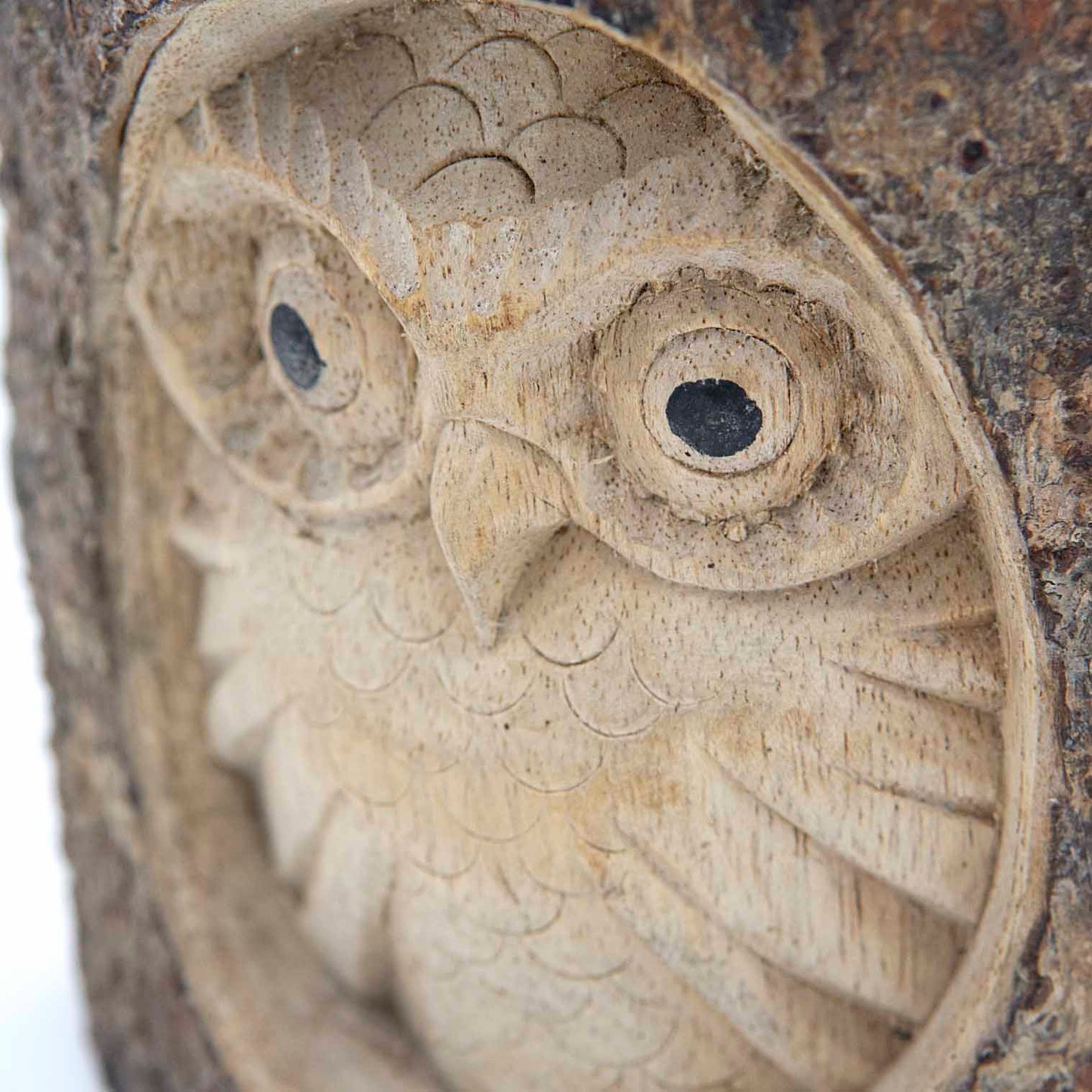 Close detail of owl face carved in pale wood showing feather scales, disc eyes and hooked beak