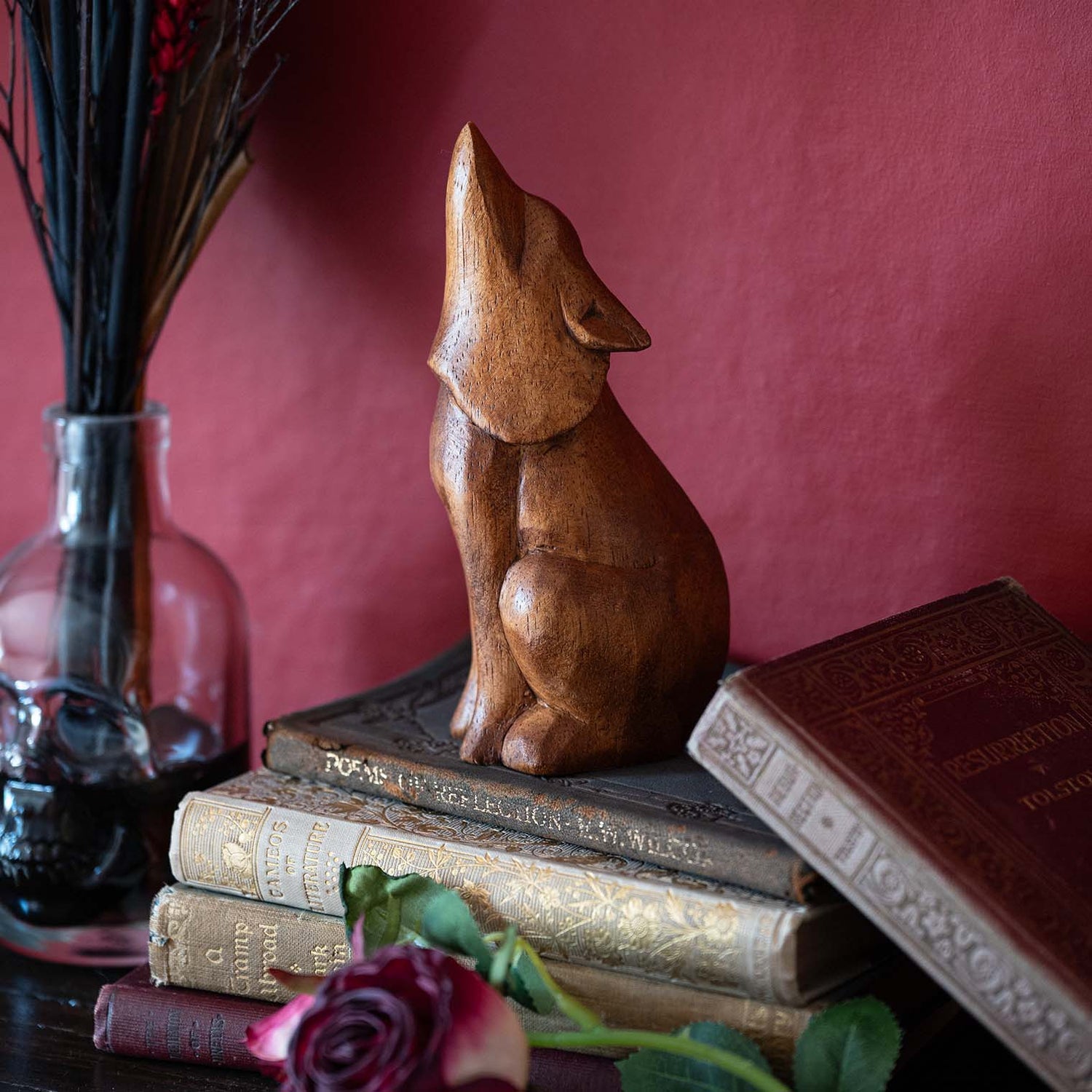 Hand-carved amber wood howling wolf figurine sitting upright on antique books beside a glass vase with dried grasses