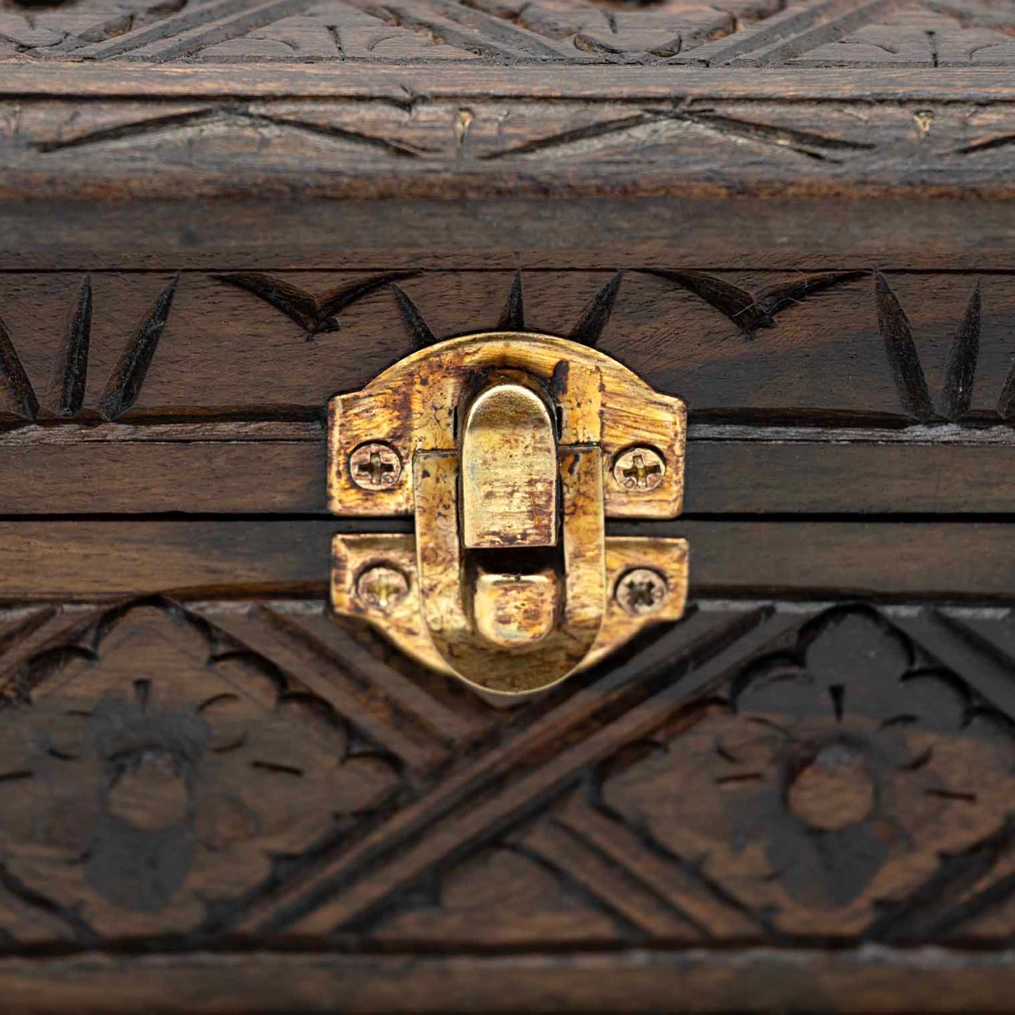 Close-up of brass toggle clasp on carved wood jewellery box with arrow-notch border carving above and below