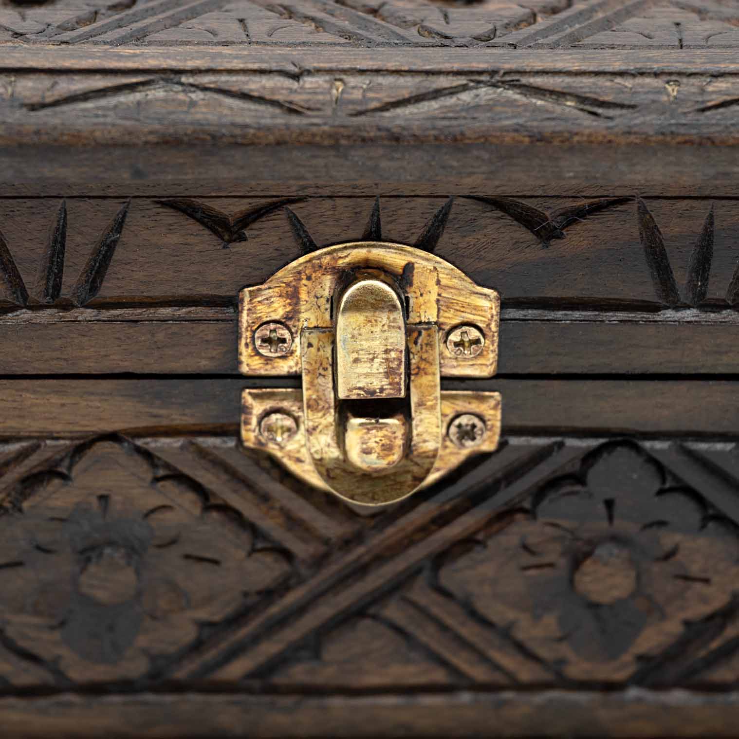 Close-up of brass toggle clasp on carved wood jewellery box with arrow-notch border carving above and below