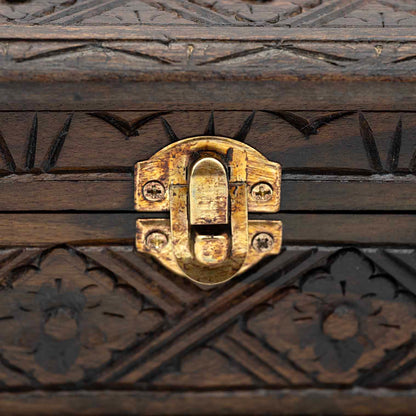 Close-up of brass toggle clasp on carved wood jewellery box with arrow-notch border carving above and below