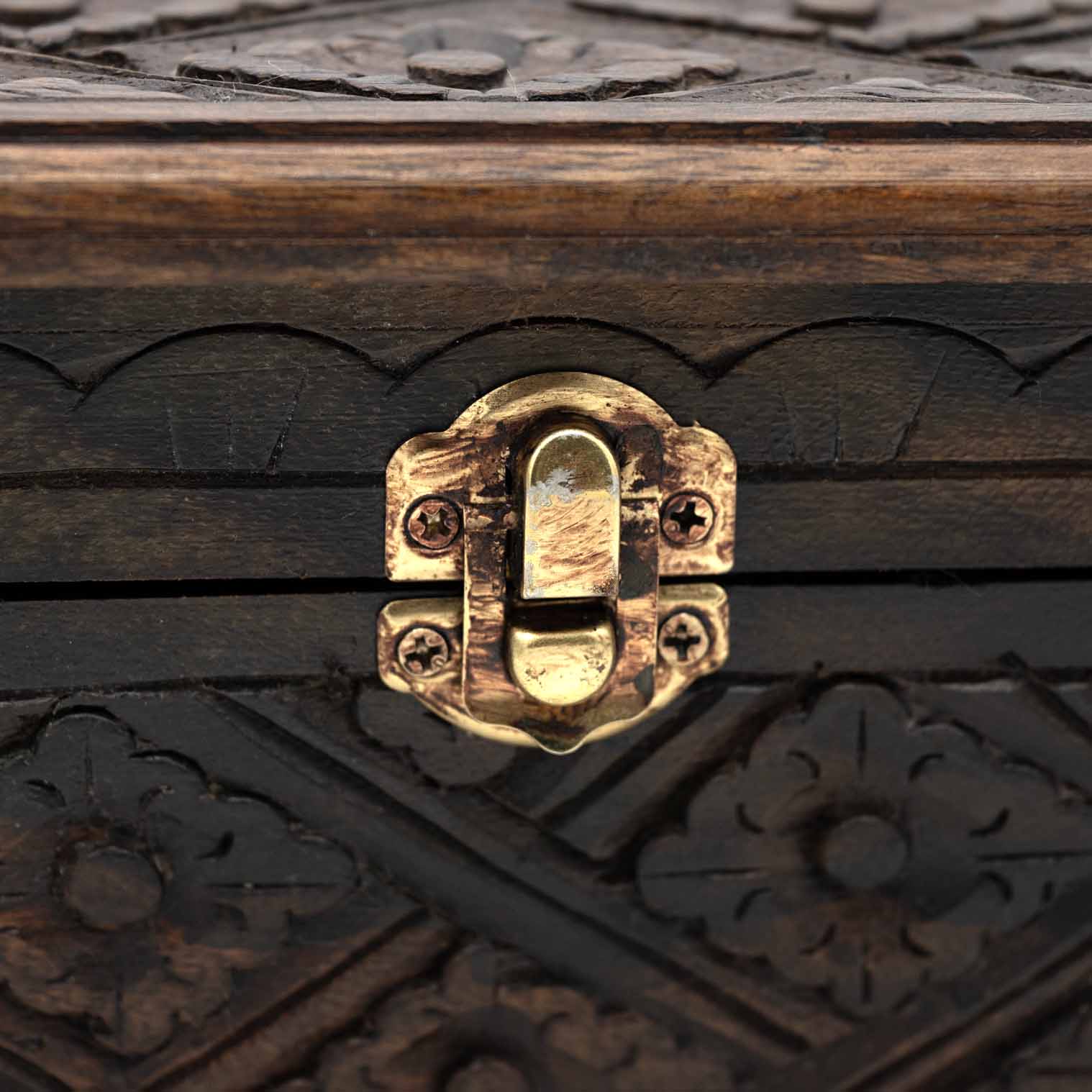 Close-up of brass toggle clasp on carved wooden jewellery chest with scallop-edge border carving above