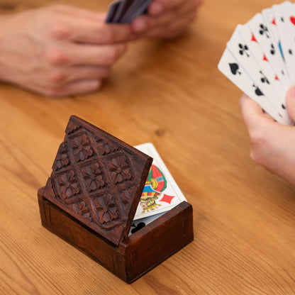 Carved wood playing card box propped open with a deck of cards inside, on a wooden table during a card game