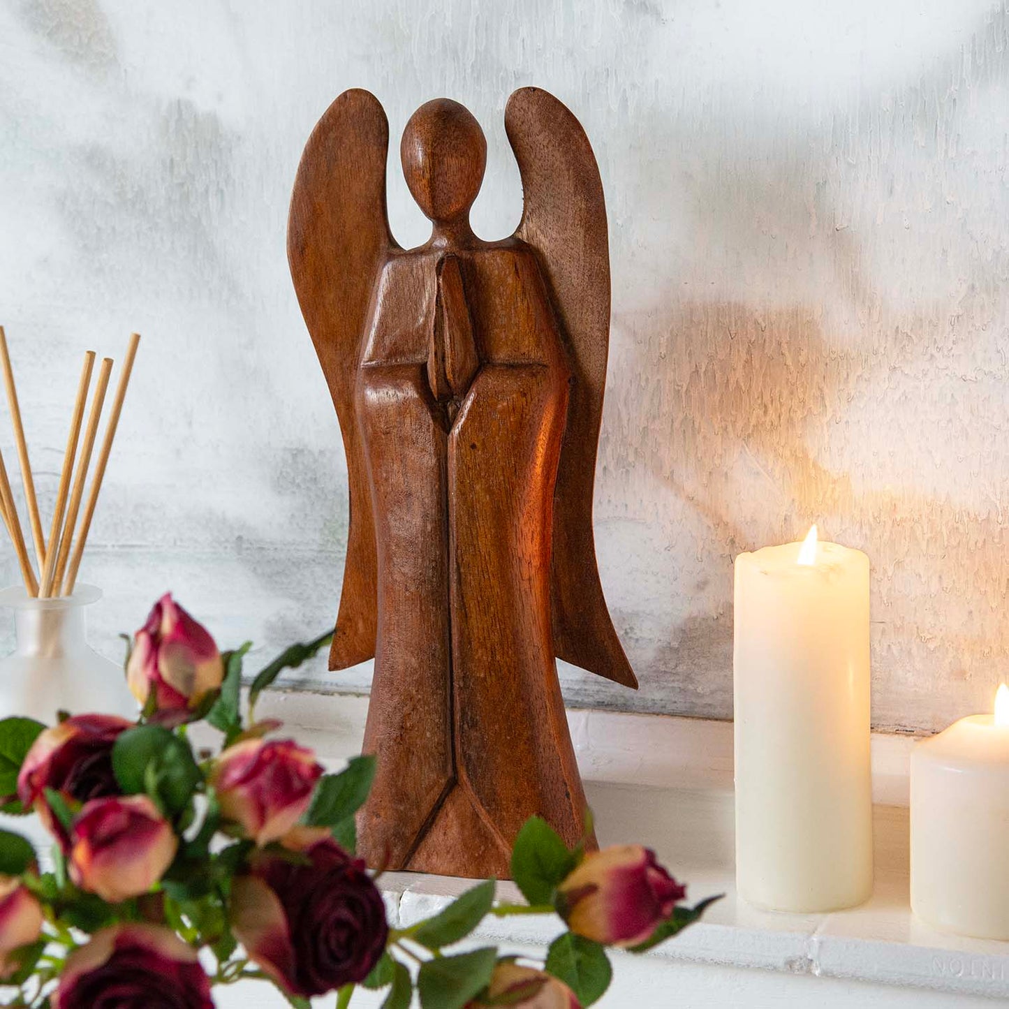 30cm abstract wooden angel carving on a mantelpiece with roses and candles, front view, Indonesia