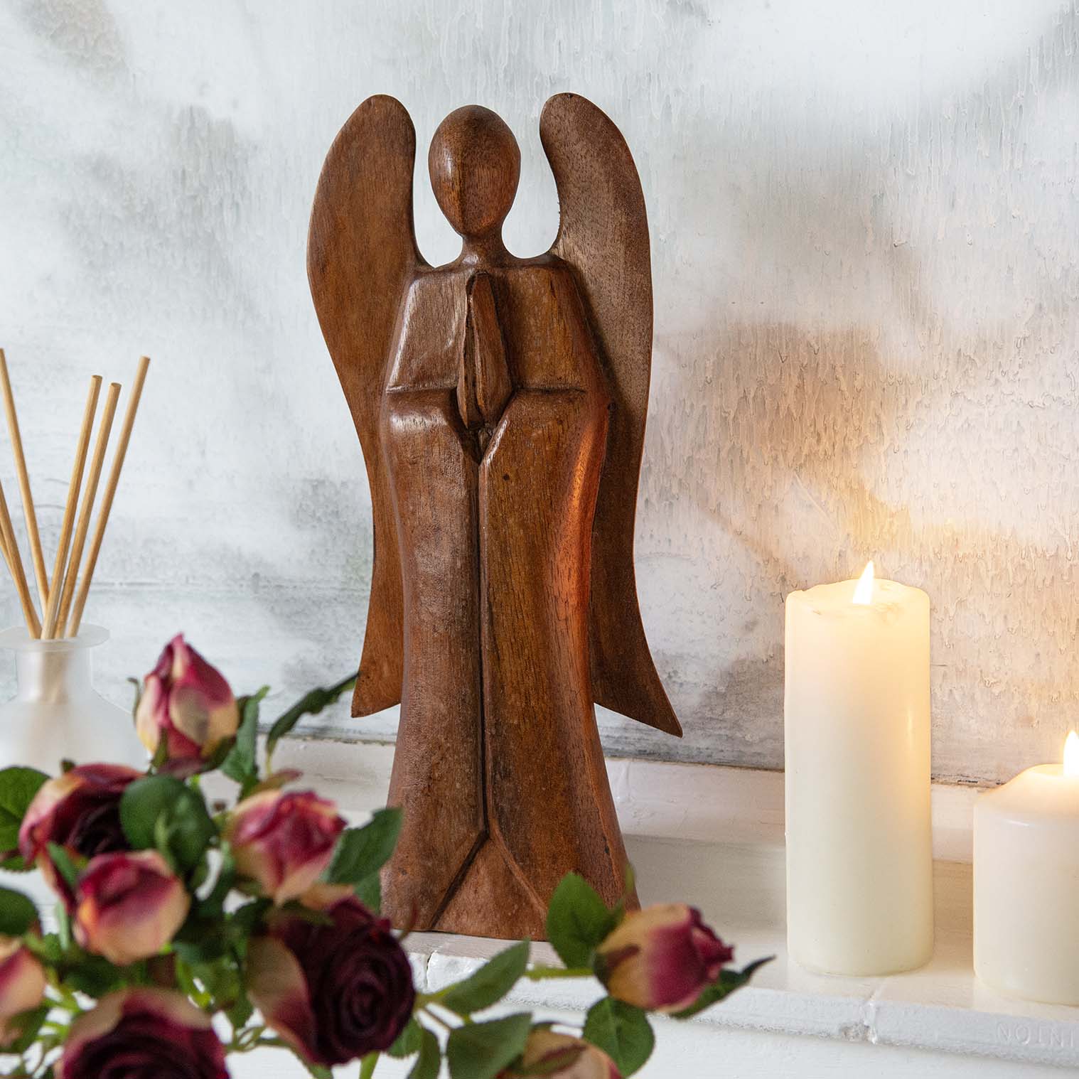 30cm abstract wooden angel carving on a mantelpiece with roses and candles, front view, Indonesia