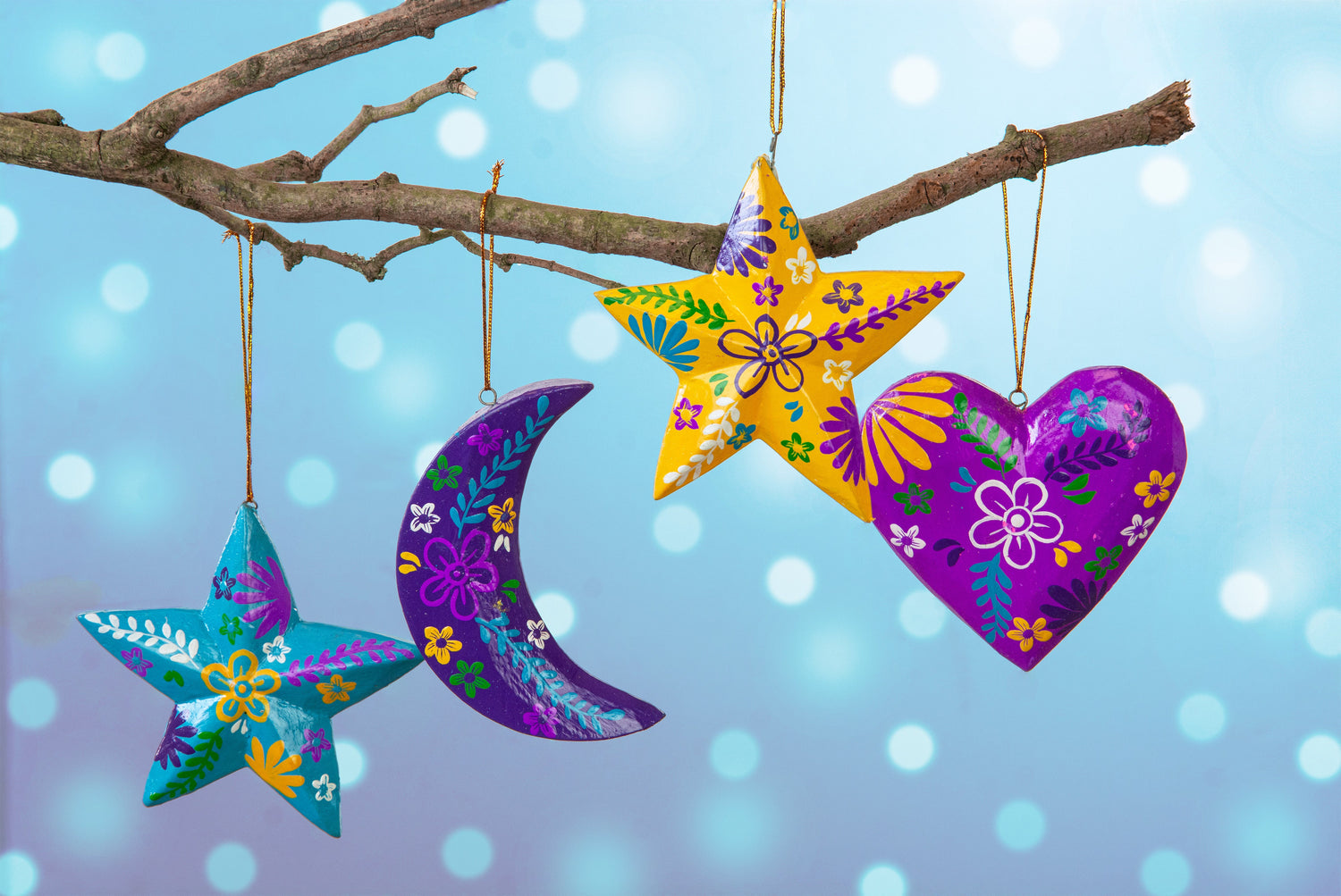 Four hand-painted wood hanging decorations on a branch: teal star, purple moon, yellow star and purple heart, Bali